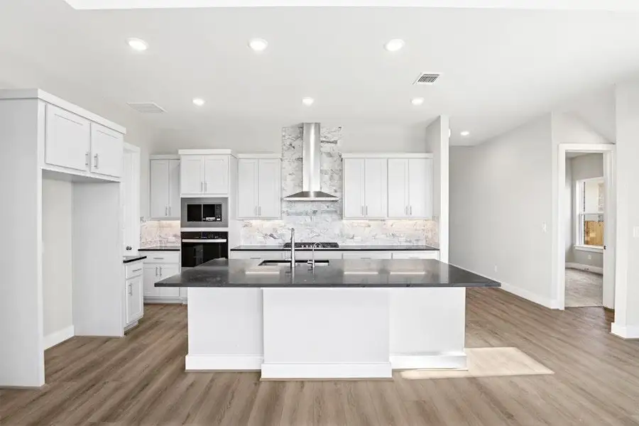 Kitchen with white cabinets, backsplash, light wood-type flooring, wall chimney exhaust hood, and stainless steel appliances Kitchen with white cabinets, backsplash, light wood-type flooring, wall chimney exhaust hood, and stainless steel appliances