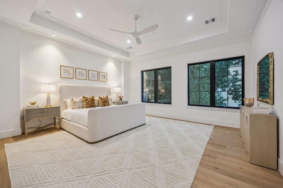 The serene bedroom is designed as a calm, light-filled retreat that blends modern simplicity with soft, inviting warmth. Architectural details such as the coffered ceiling and modern ceiling fan add dimension and functionality without overwhelming the space. Clean lines, reading lights, and warm woods, complete this beautiful room.