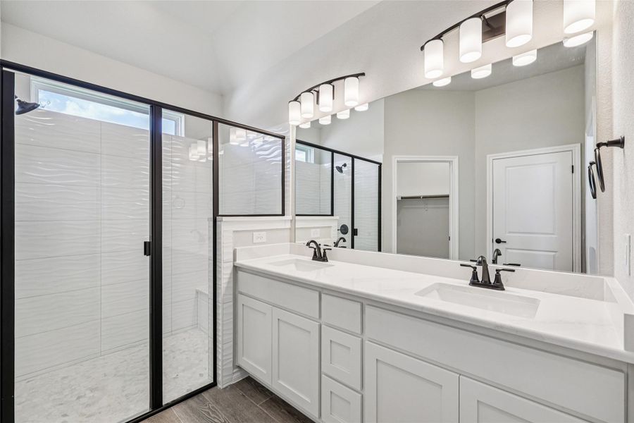 Full bathroom with a stall shower, double vanity, wood finished floors, and a spacious closet Full bathroom with a stall shower, double vanity, wood finished floors, and a spacious closet