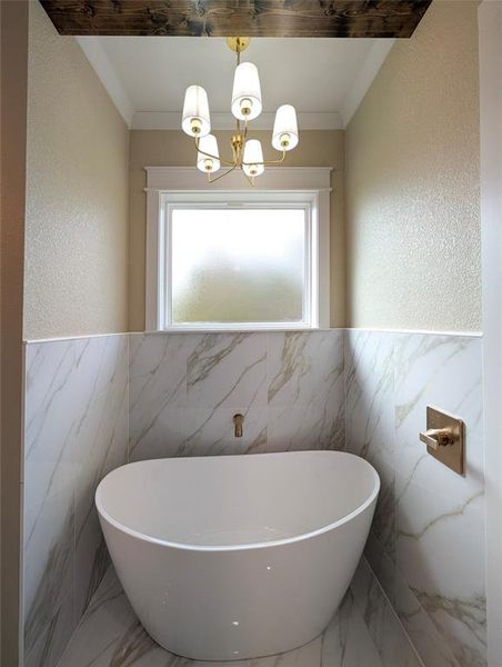 Bathroom with tile walls, wainscoting, marble tiled floors, a freestanding tub, and a chandelier