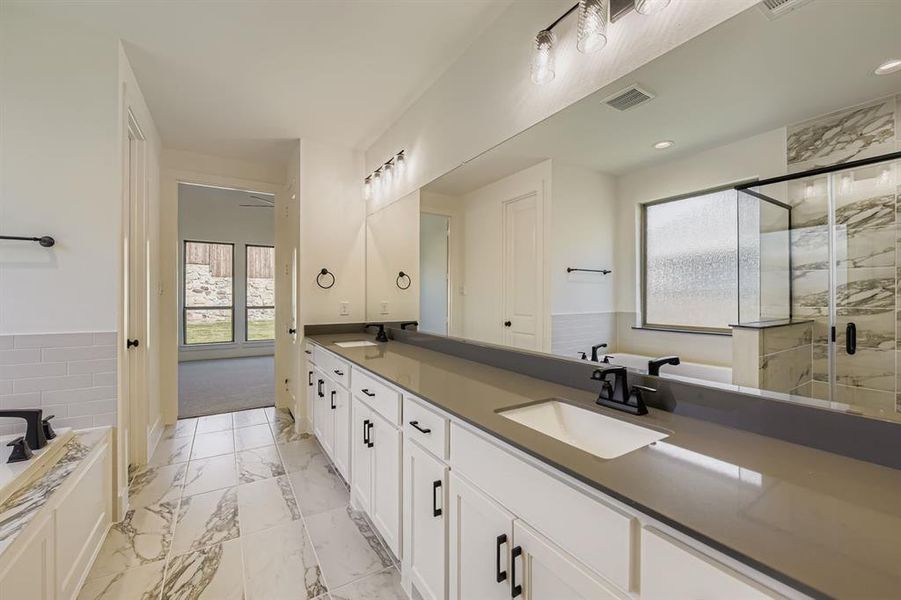 Full bathroom with double vanity, a garden tub, a marble finish shower, light marble finish floors, and wainscoting