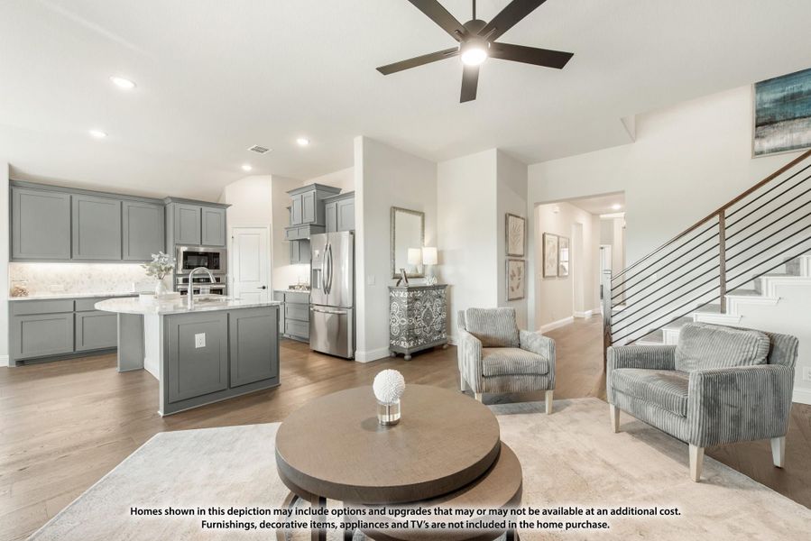 Open-concept living area and kitchen with gray cabinets, island, staircase, and ceiling fan on hardwood floors Open-concept living area and kitchen with gray cabinets, island, staircase, and ceiling fan on hardwood floors