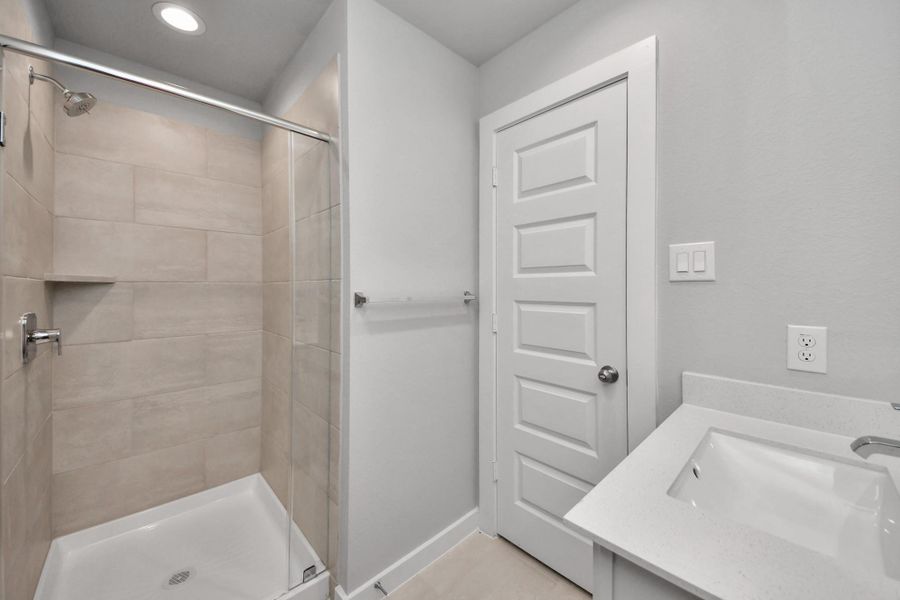 Secondary bath features tile flooring, walk-in shower with tile surround, light stained wood cabinets, beautiful light countertop.
