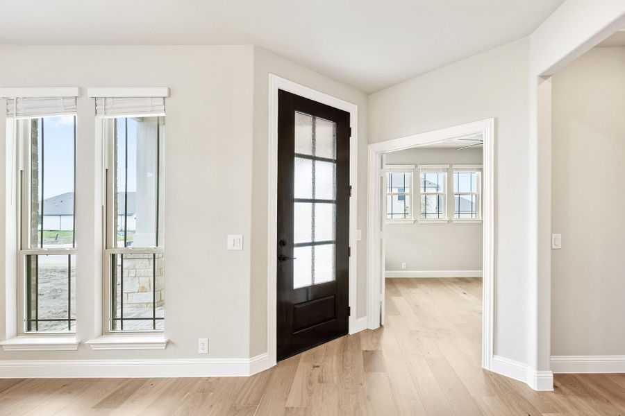 Entryway with black glass-panel door, light hardwood floors, and white trim leading to adjacent room