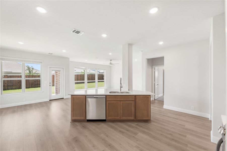 Kitchen island with sink and dishwasher, open to living area with light wood floors and large windows