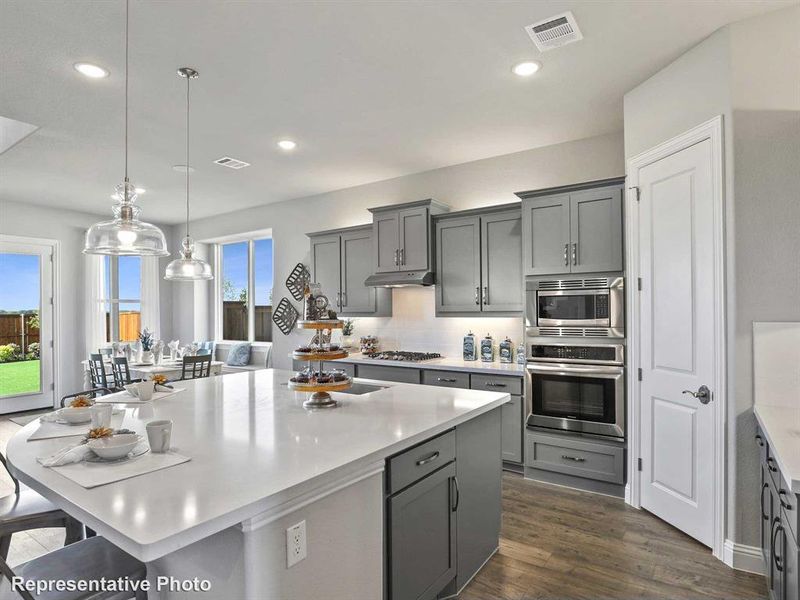 Kitchen featuring a large island with a light-toned countertop, gray cabinetry, stainless steel appliances, and wood-finish flooring
