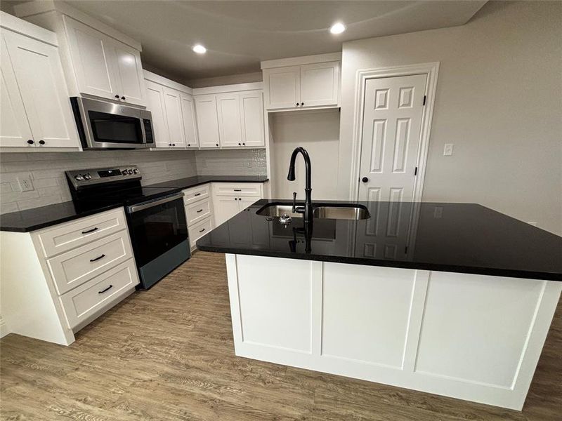 Kitchen featuring appliances with stainless steel finishes, decorative backsplash, light wood-style flooring, an island with sink, and recessed lighting