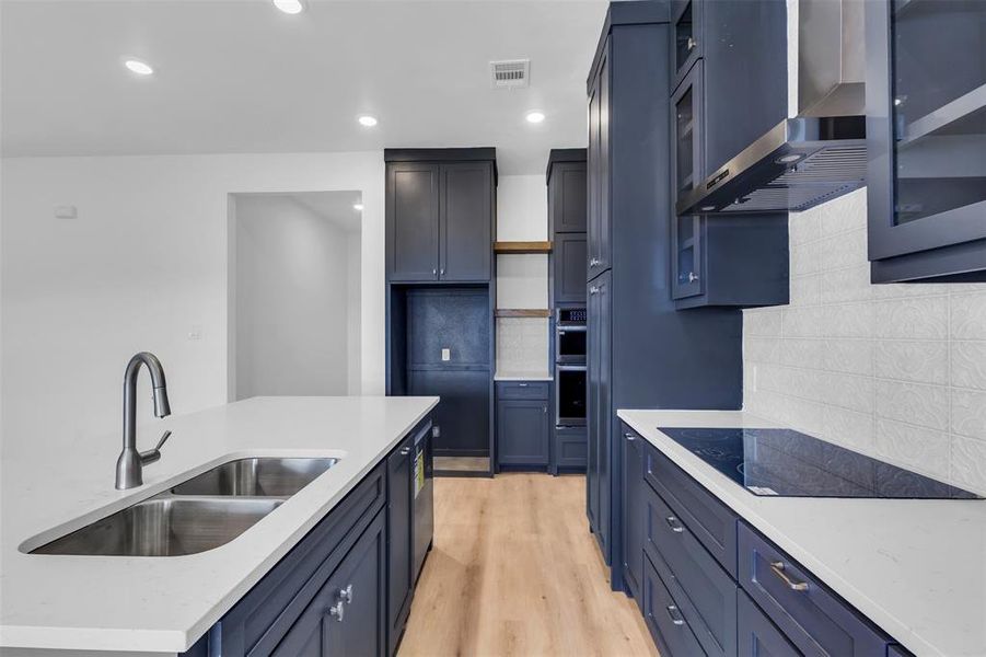 Kitchen with decorative backsplash, light wood-type flooring, wall chimney exhaust hood, black electric cooktop, and sink