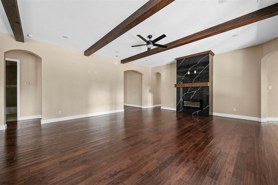 Unfurnished living room featuring a premium fireplace, hardwood / wood-style floors, and beam ceiling