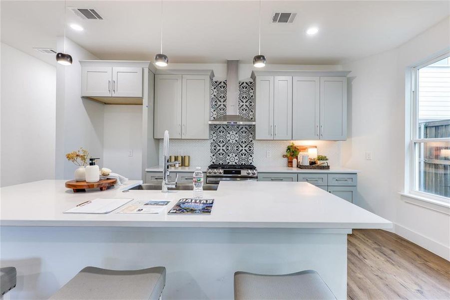 Kitchen with pendant lighting, stainless steel stove, a breakfast bar area, and wall chimney exhaust hood