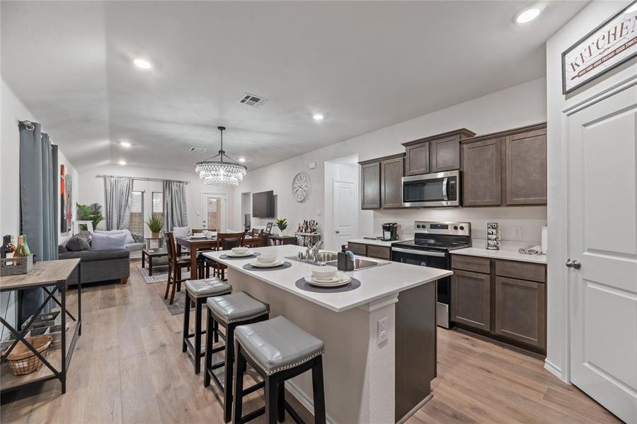 Kitchen with stainless steel appliances, a kitchen breakfast bar, recessed lighting, dark brown cabinetry, and light wood-style floors