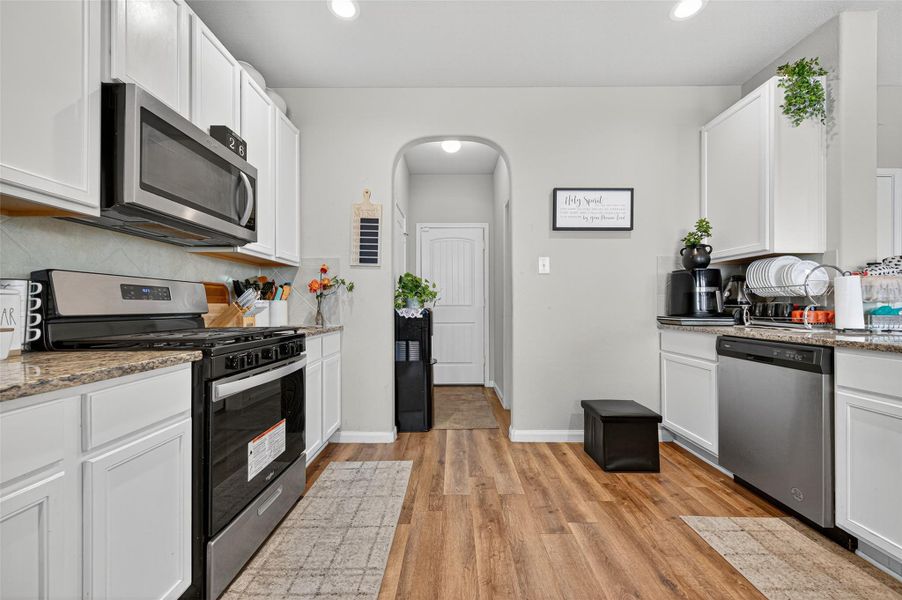 Modern kitchen with stainless steel appliances, white cabinetry, and wood flooring. Features a cozy layout with ample counter space and natural light.