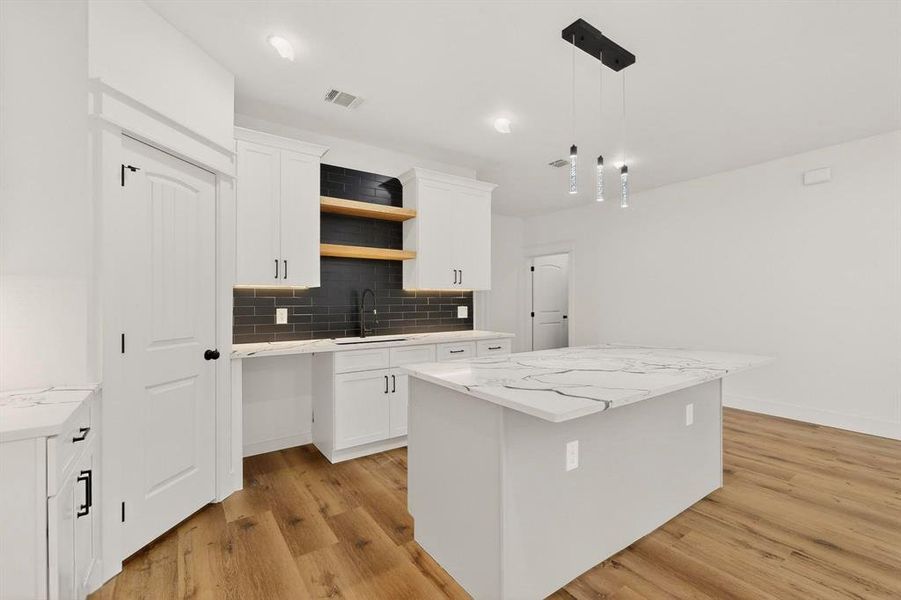 Kitchen featuring a center island, light wood-style flooring, light stone countertops, decorative backsplash, and white cabinets Kitchen featuring a center island, light wood-style flooring, light stone countertops, decorative backsplash, and white cabinets