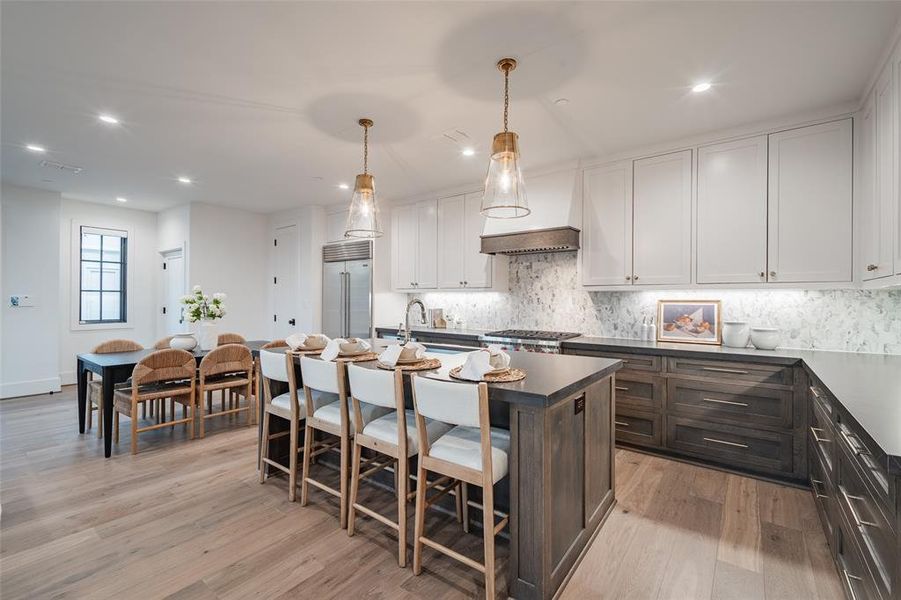 Kitchen featuring light wood-type flooring, a kitchen island with sink, pendant lighting, white cabinetry, and built in refrigerator