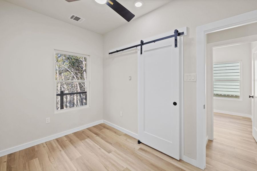 Unfurnished bedroom with a barn door, light wood-style flooring, and ceiling fan Unfurnished bedroom with a barn door, light wood-style flooring, and ceiling fan
