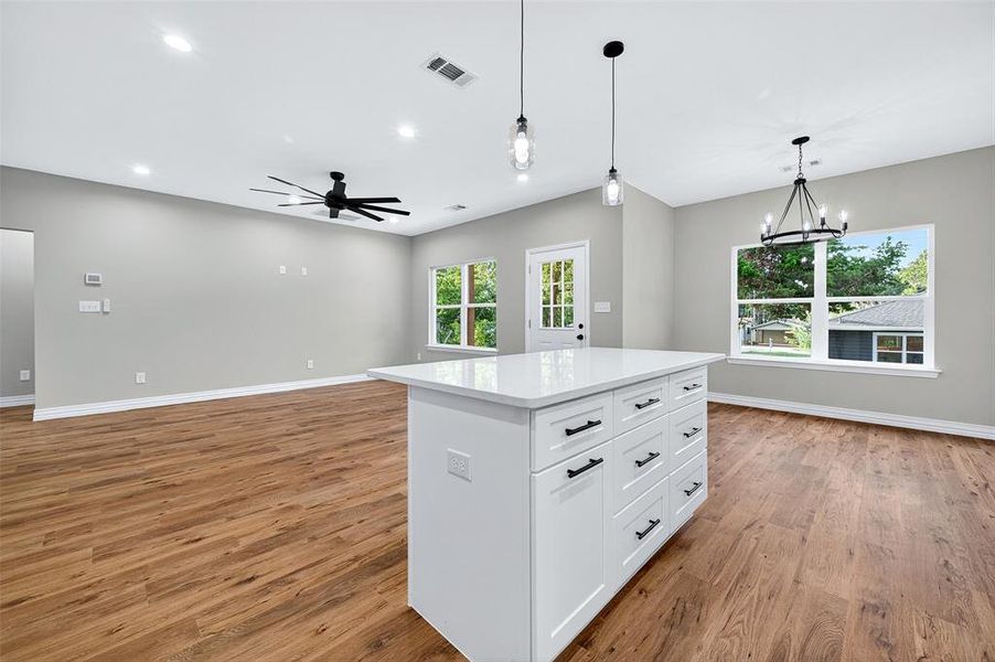 Kitchen with pendant lighting, white cabinetry, open floor plan, a center island, and light wood-style floors Kitchen with pendant lighting, white cabinetry, open floor plan, a center island, and light wood-style floors
