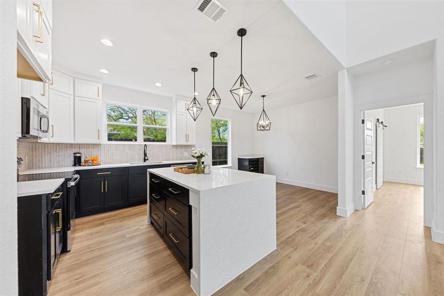 The kitchen features dark lower cabinets with gold hardware, white upper cabinets, and a white countertop on the island The kitchen features dark lower cabinets with gold hardware, white upper cabinets, and a white countertop on the island