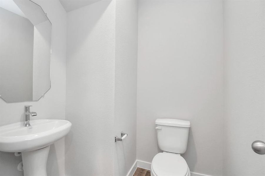 Delightful half bathroom featuring a sophisticated 5-panel door, upgraded pedestal sink, contemporary hardware, and bright recessed lights. Sample photo of completed home with same plan. Actual colors and selections may vary.