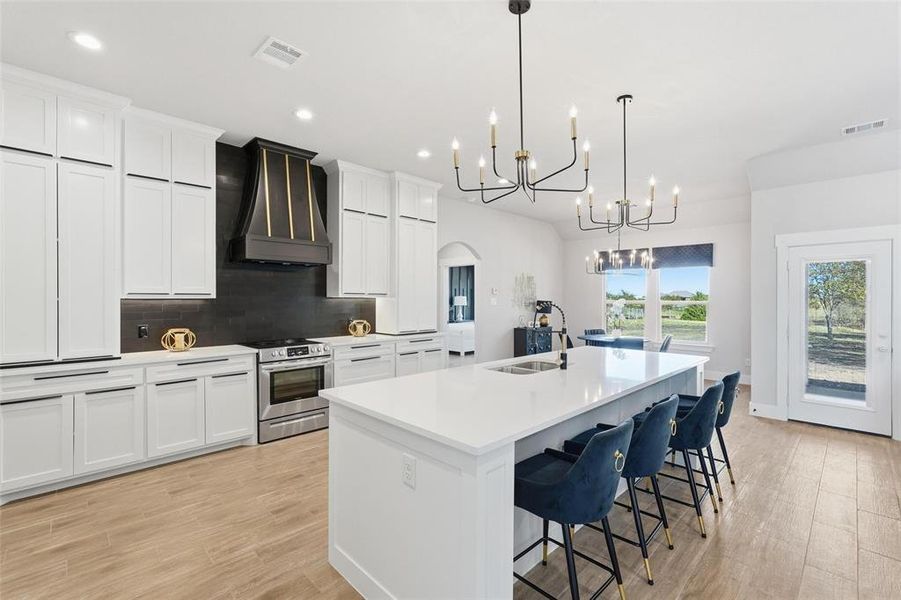 Kitchen with arched walkways, tasteful backsplash, custom exhaust hood, white cabinetry, and recessed lighting