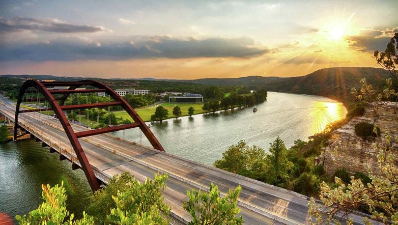 Austin, Texas scenic view taken at sunset with the sun peeking out from behind the clouds, water flowing down the river, and a roadway bridge in the forefront Austin, Texas scenic view taken at sunset with the sun peeking out from behind the clouds, water flowing down the river, and a roadway bridge in the forefront