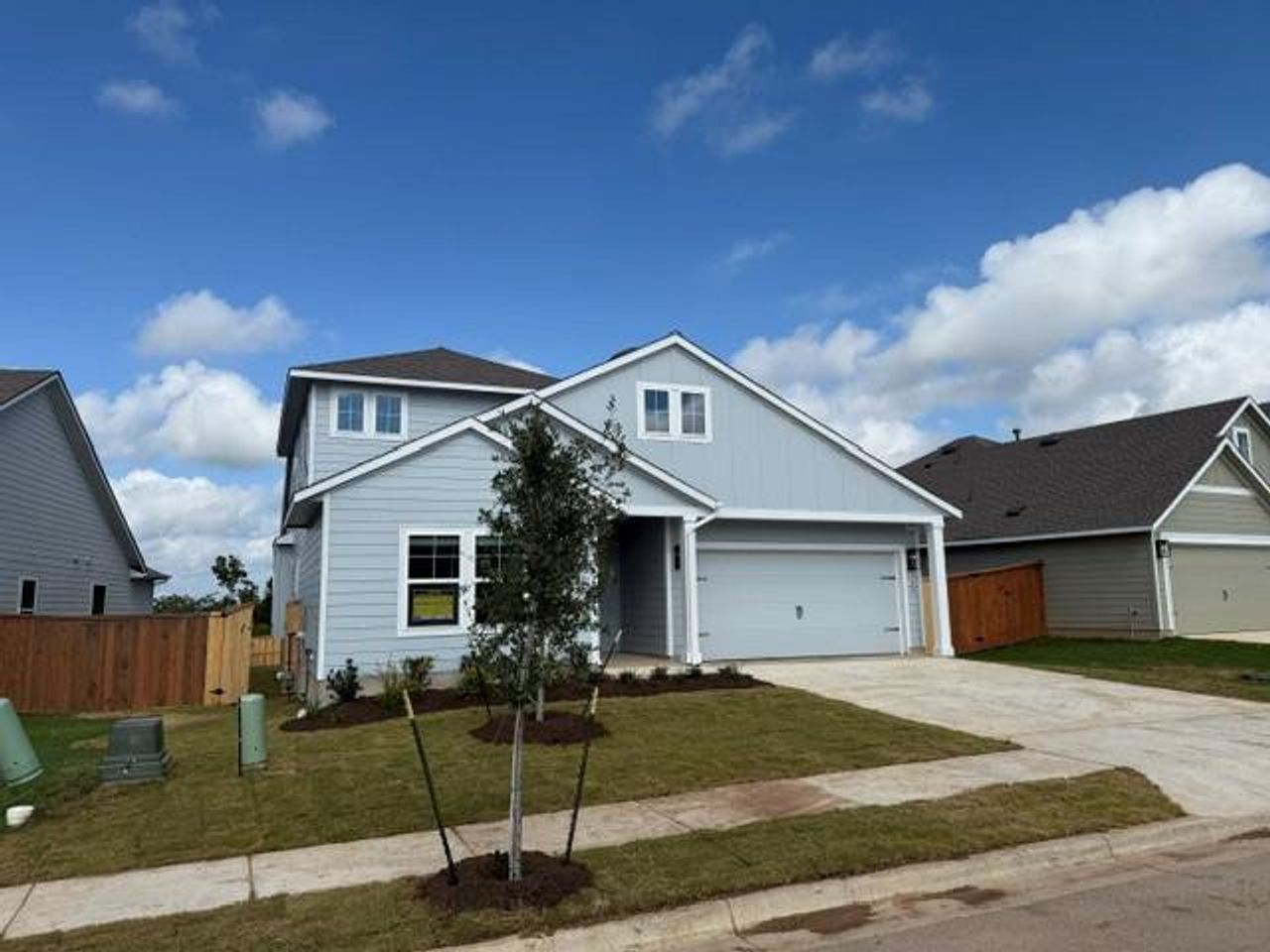 A newly constructed residence features light blue siding, an attached garage, and a newly seeded front yard.