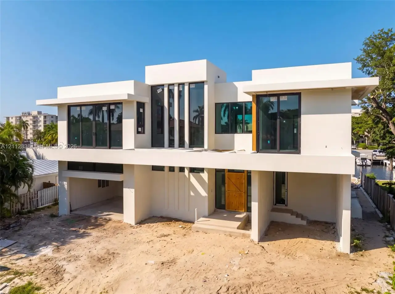 Modern two-story architectural exterior featuring smooth stucco siding, large-format glass windows, a cantilevered second-story balcony, and an integrated multi-car parking area Modern two-story architectural exterior featuring smooth stucco siding, large-format glass windows, a cantilevered second-story balcony, and an integrated multi-car parking area