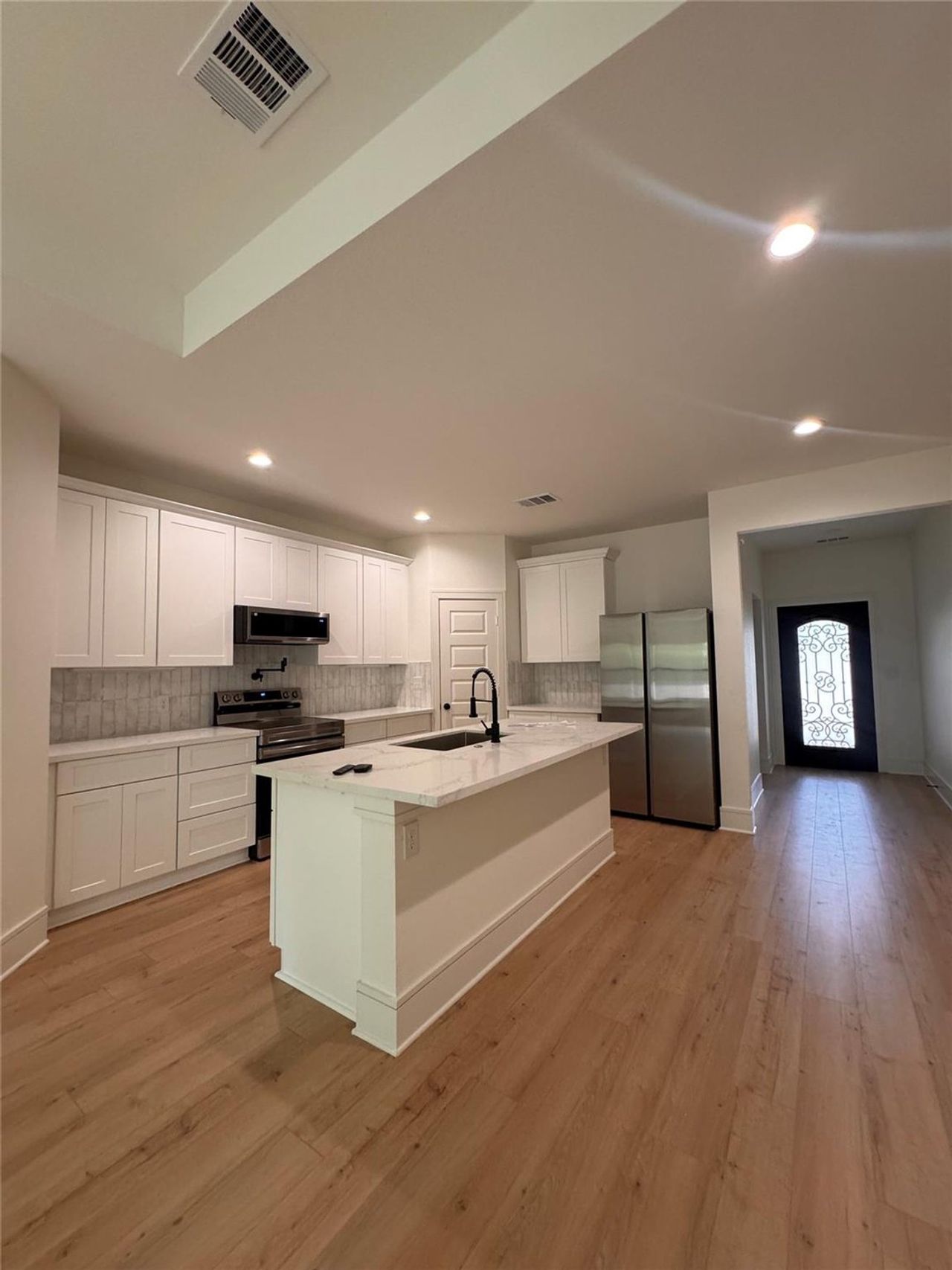 Kitchen featuring stainless steel appliances, a center island with sink, white cabinets, light stone countertops, and light wood-style flooring