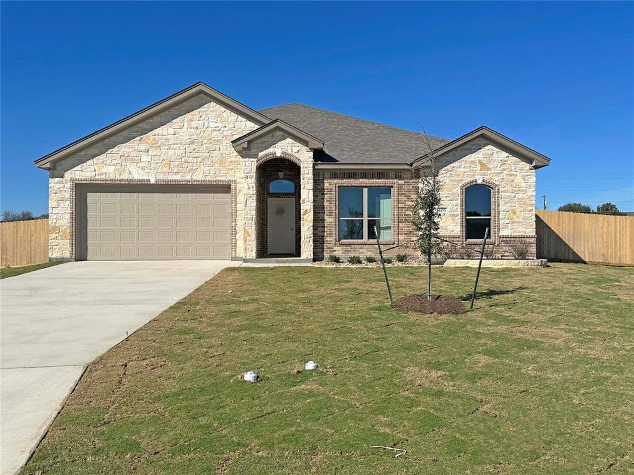 French provincial home with stone siding, driveway, a garage, and roof with shingles