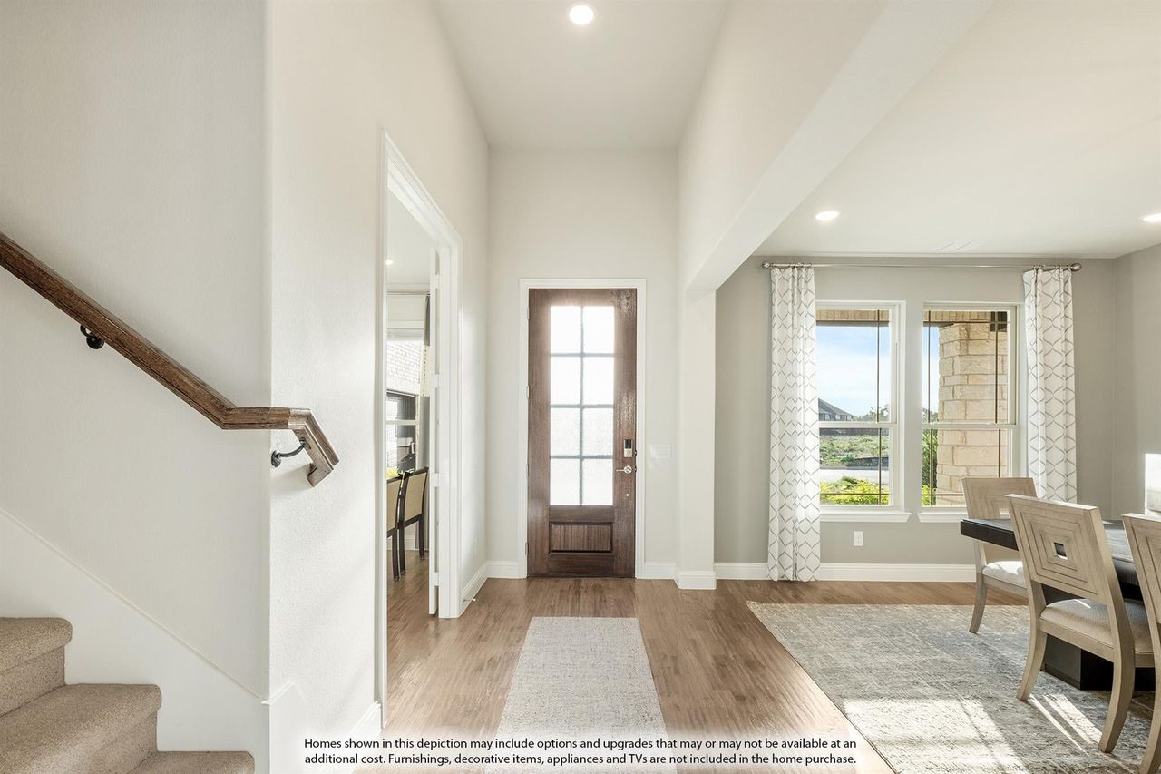 Bright home entryway with wood front door, hardwood floors, staircase, and dining area with large windows