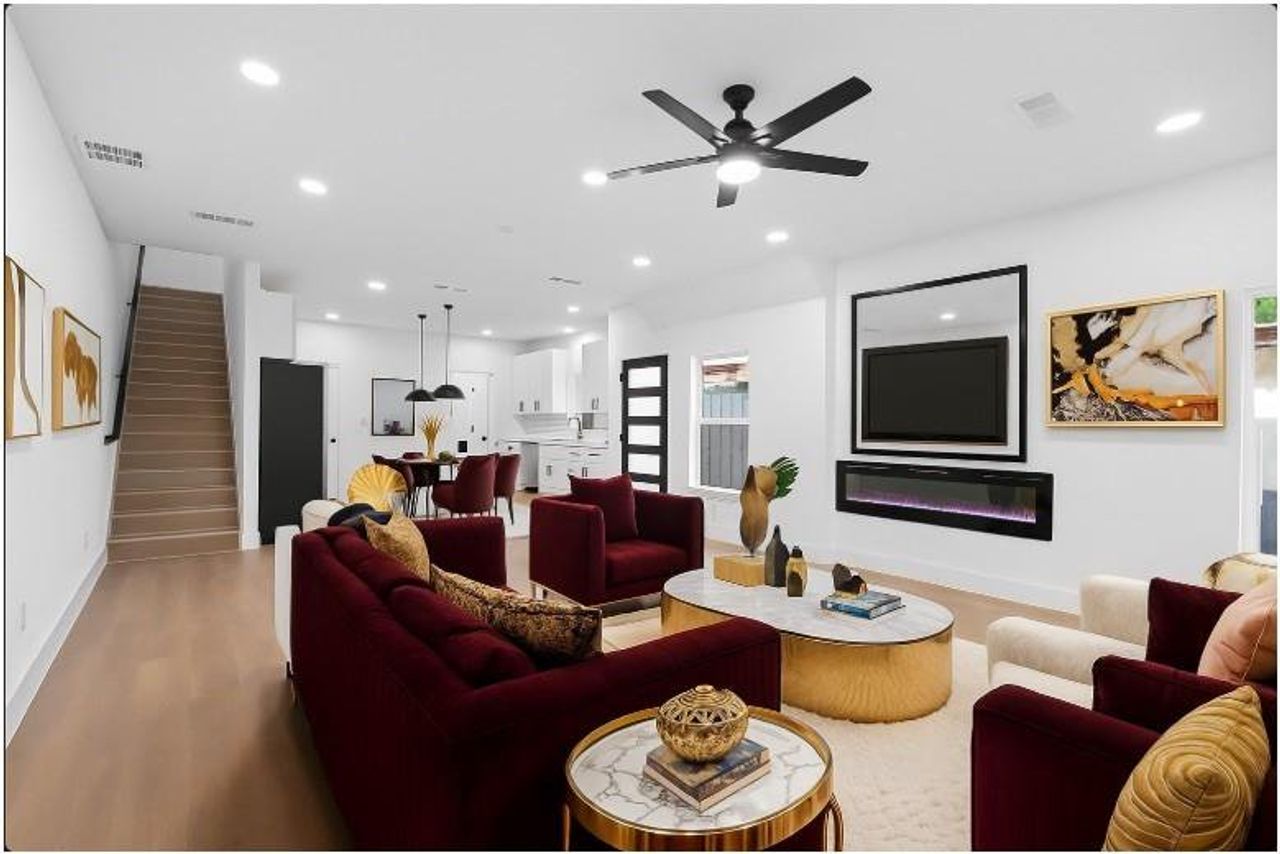Living room with light wood-style floors, a glass covered fireplace, stairs, recessed lighting, and a ceiling fan