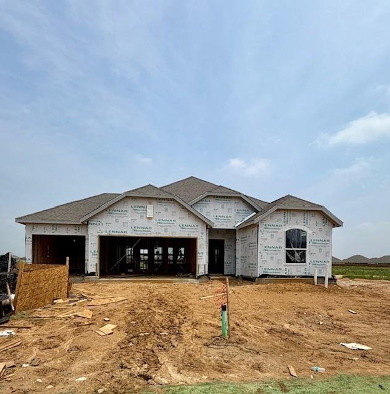 New construction home framed and wrapped, featuring a multi-gabled roofline, an arched window, and a three-car garage opening
