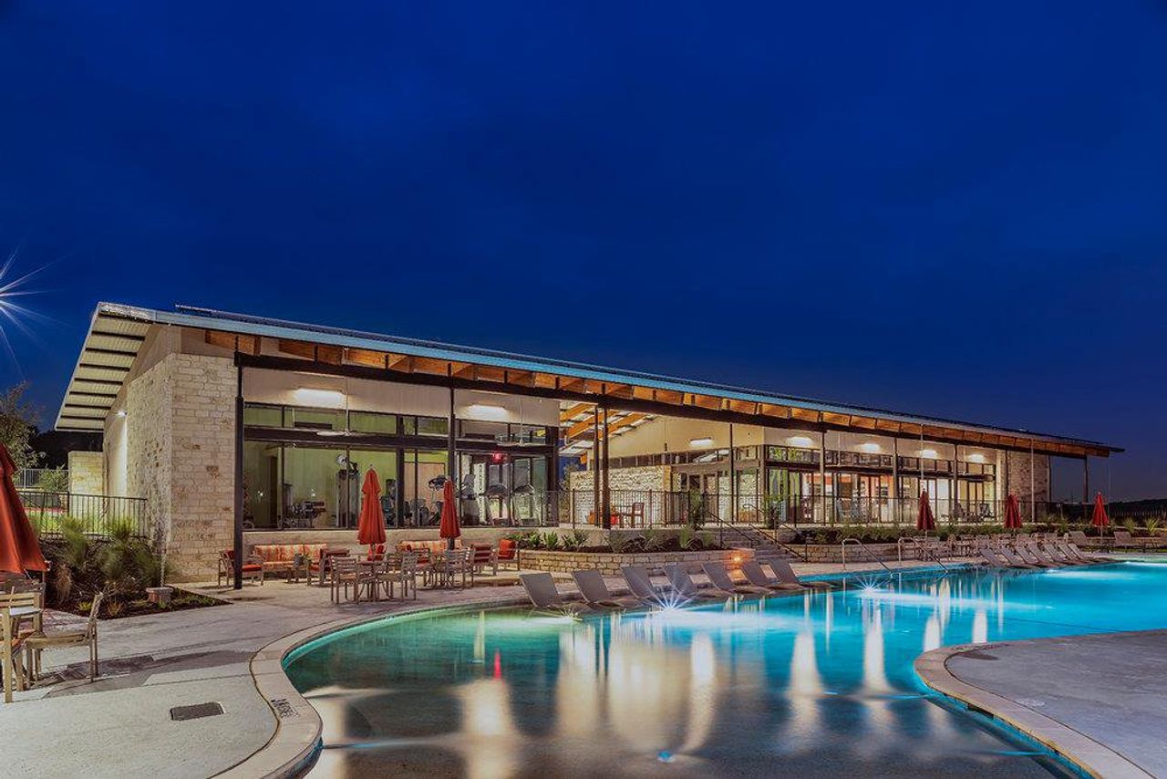 An expansive outdoor swimming pool sits adjacent to a modern stone clubhouse under evening skies.