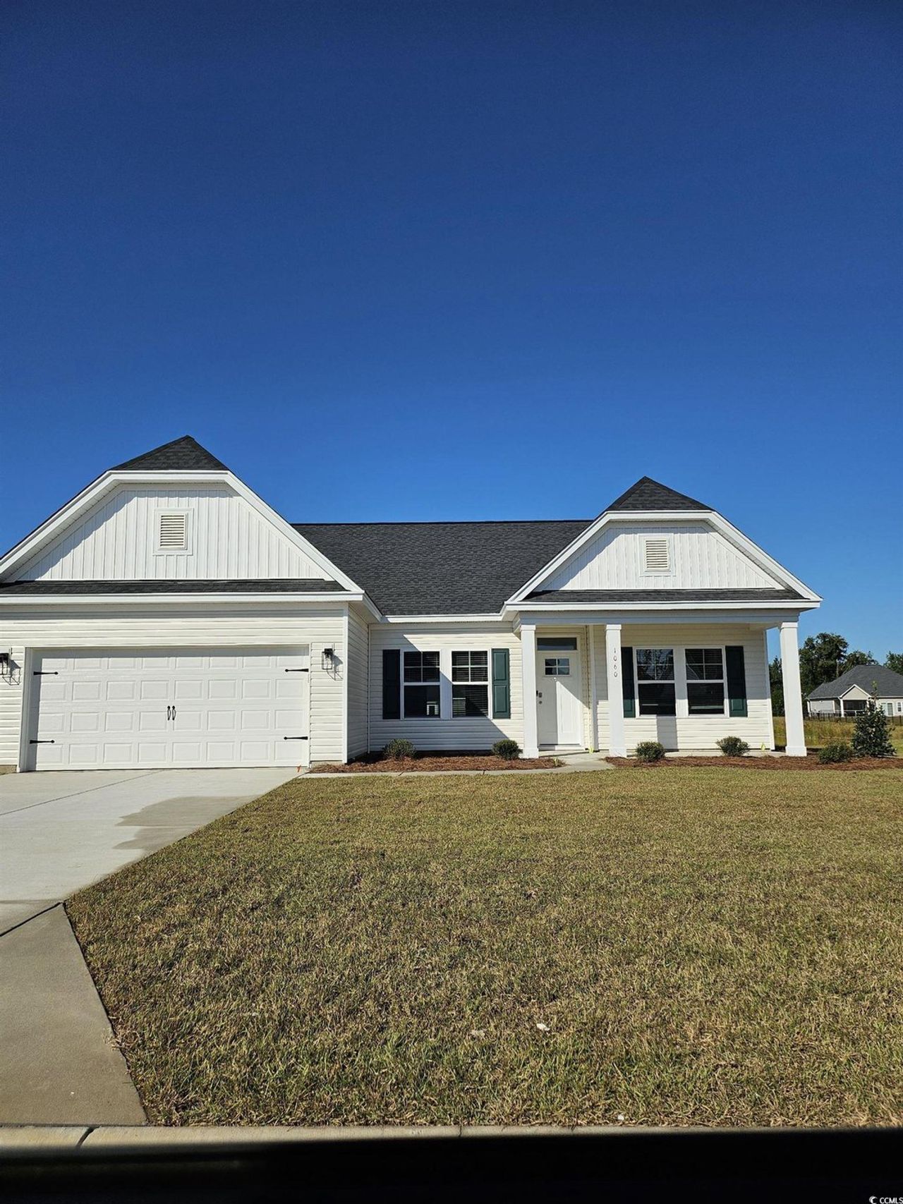 View of front of house featuring covered porch, driveway, an attached garage, a front yard, and roof with shingles