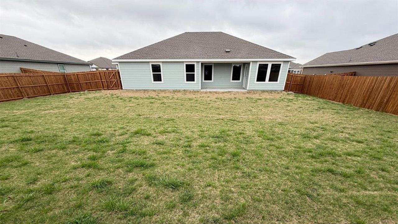 Expansive grassed backyard featuring a wooden privacy fence, a concrete patio, and light blue siding