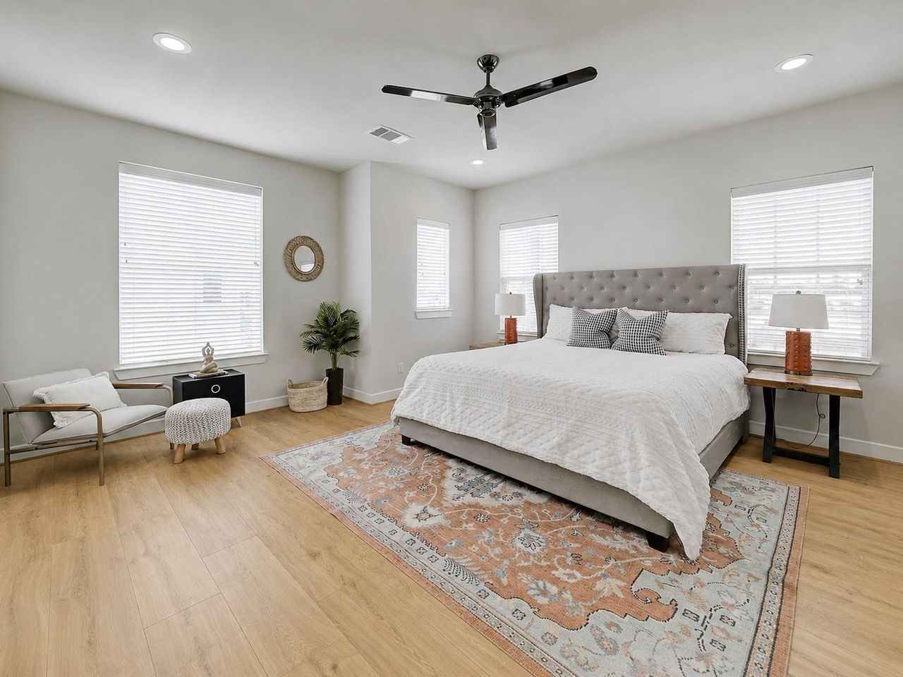 Primary bedroom sanctuary — tufted king bed centerpiece, rich wood-look flooring, multiple accent windows streaming soft natural light, and space for a cozy reading nook. Primary bedroom sanctuary — tufted king bed centerpiece, rich wood-look flooring, multiple accent windows streaming soft natural light, and space for a cozy reading nook.