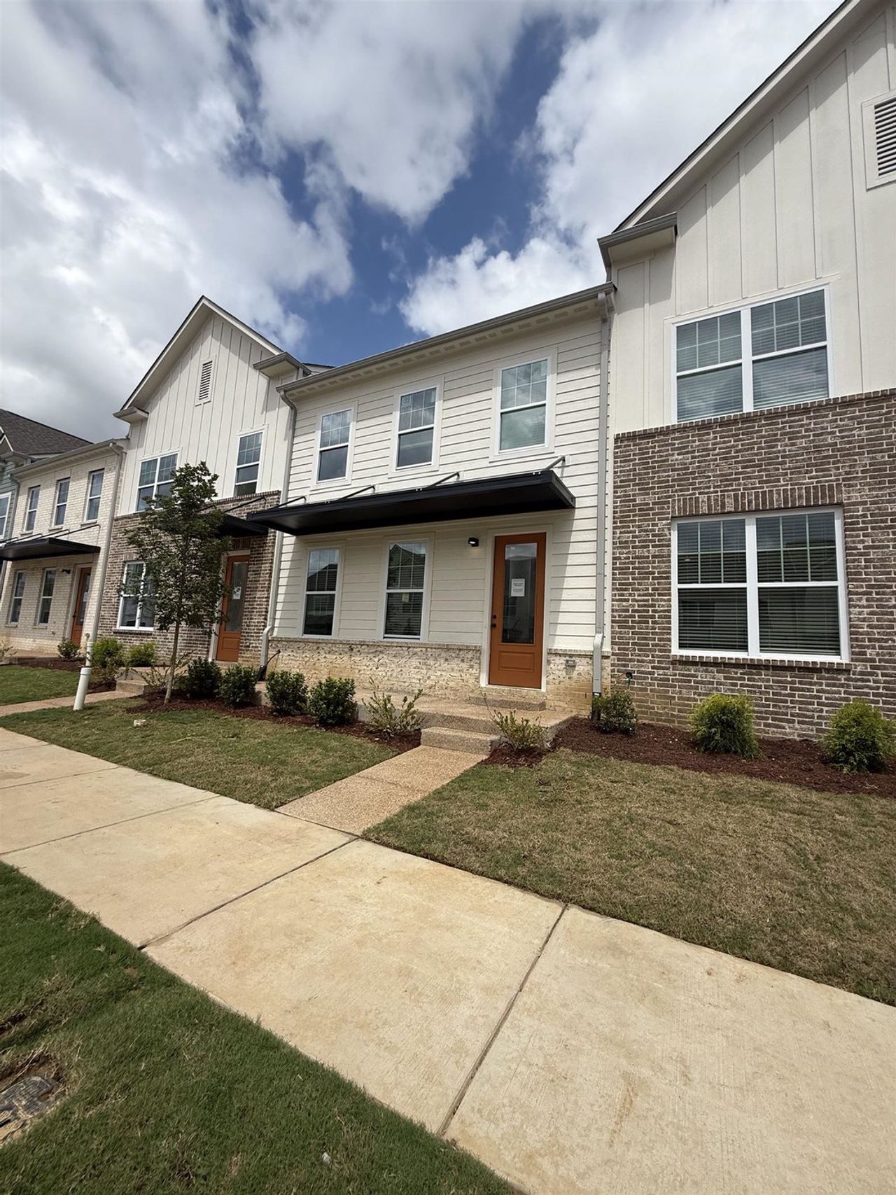 Modern townhome exterior featuring light-colored siding, dark brick accents, and a distinctive front awning
