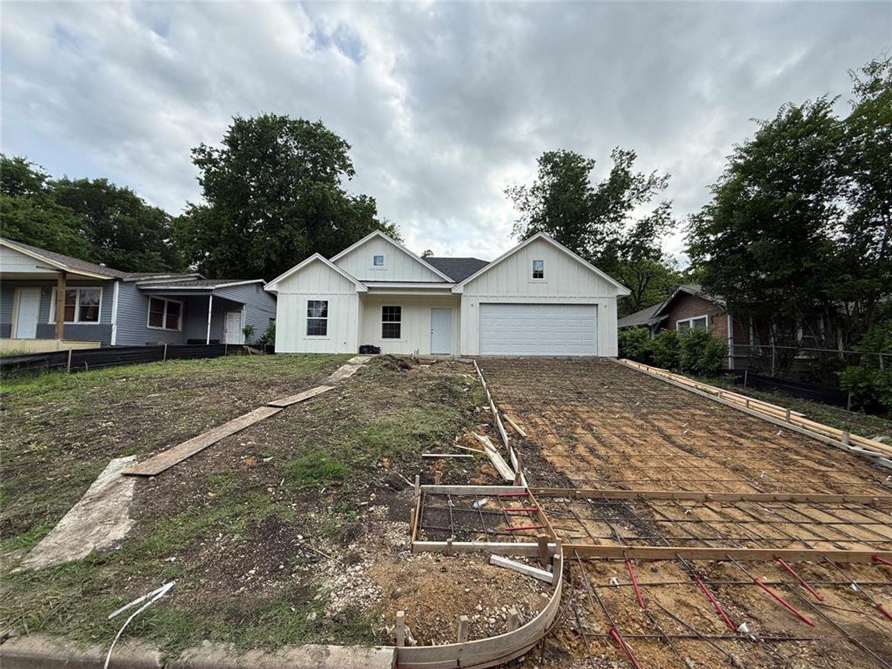 Contemporary white siding residence featuring a two-car garage, dark shingle roof, and a developing concrete driveway