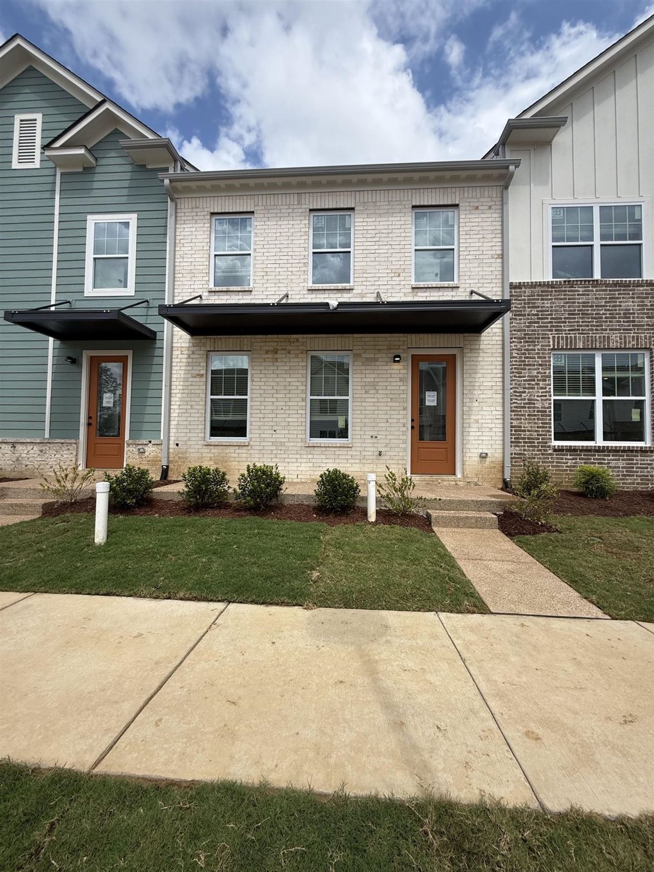 White brick facade featuring a brown wood-finish entry door with modern black awning