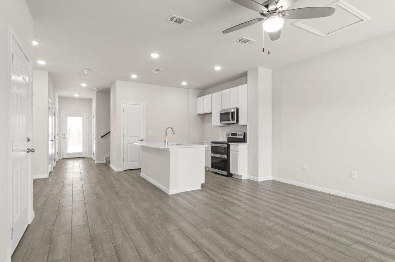 Kitchen featuring an island with sink, stainless steel appliances, white cabinetry, ceiling fan, and open floor plan