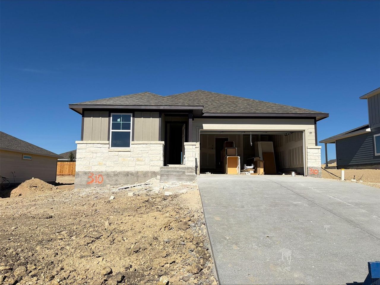 View of front facade featuring stone siding, roof with shingles, driveway, and a garage