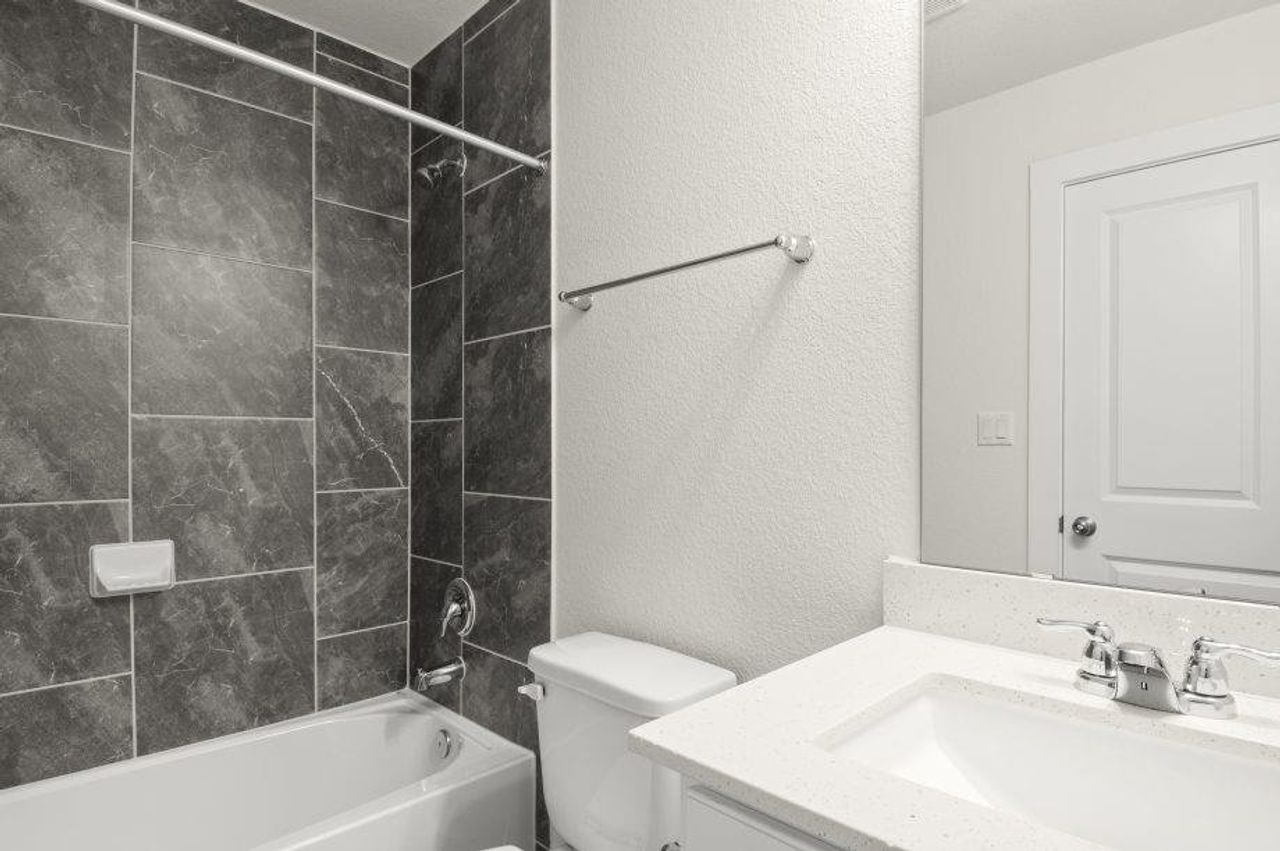 Modern bath features sleek tiled walls, a pristine tub, and a vanity with a polished basin.