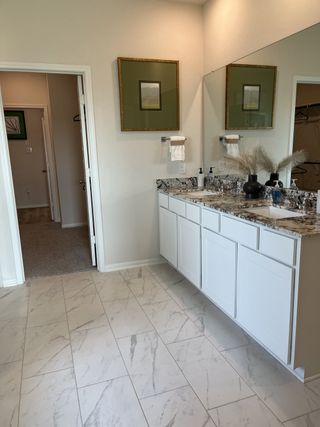 A modern bathroom showcasing marble tile flooring, granite countertops, and sleek white cabinetry with elegant decor.