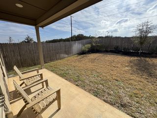 A cozy patio with wooden chairs overlooking a grassy yard and fence.