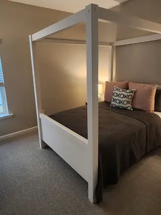 A cozy bedroom with a canopy bed, soft brown bedding, and modern lighting accents on a plush carpet.