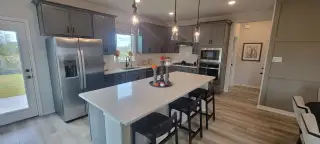 A modern kitchen with sleek gray cabinets, a large island, stainless steel appliances, and stylish pendant lighting.