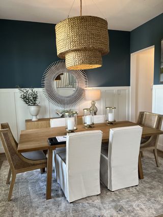 A chic dining room with a large woven pendant light, elegant furnishings, and a textured mirror on a deep blue accent wall.