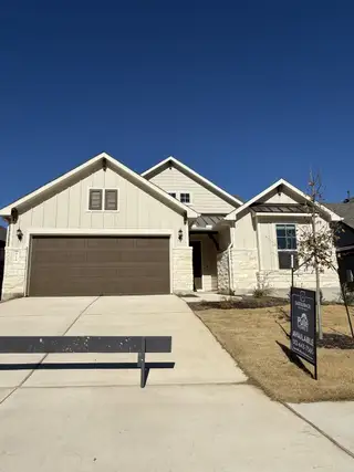 Charming beige stone home with a spacious driveway in Saddleback at Santa Rita Ranch by Pulte Homes (Liberty Hill, TX).