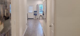 Model Home A spacious hallway with wood flooring, creamy beige walls, and bright natural light from windows and a glass-paneled door.