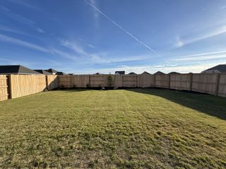 A spacious fenced backyard under a clear sky in The Colony 50s by Ashton Woods (Bastrop, TX).