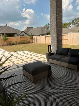 A serene patio with modern outdoor furniture, patterned rug, and spacious backyard under a partly cloudy sky.